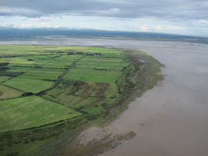Eroded edge of the saltmarsh at Cardurnock, with Moricambe Bay beyond and the Lakeland fells; the masts of Anthorn to the right